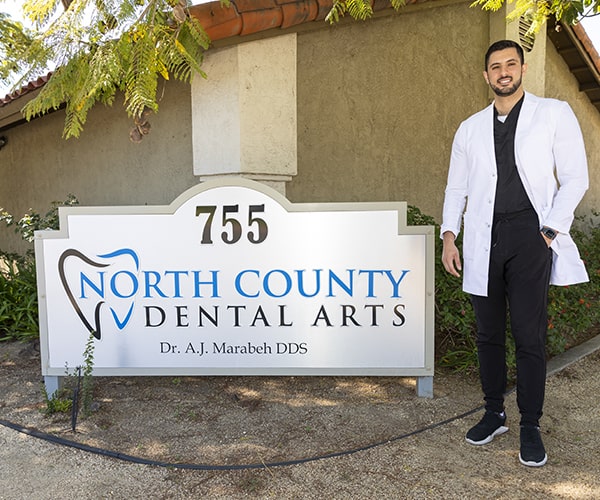 Dr. Marabeh outside his dental office next to the North Country Dental Arts sign