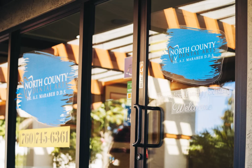 Glass front doors of North County Dental Arts showing the practice logo and phone number